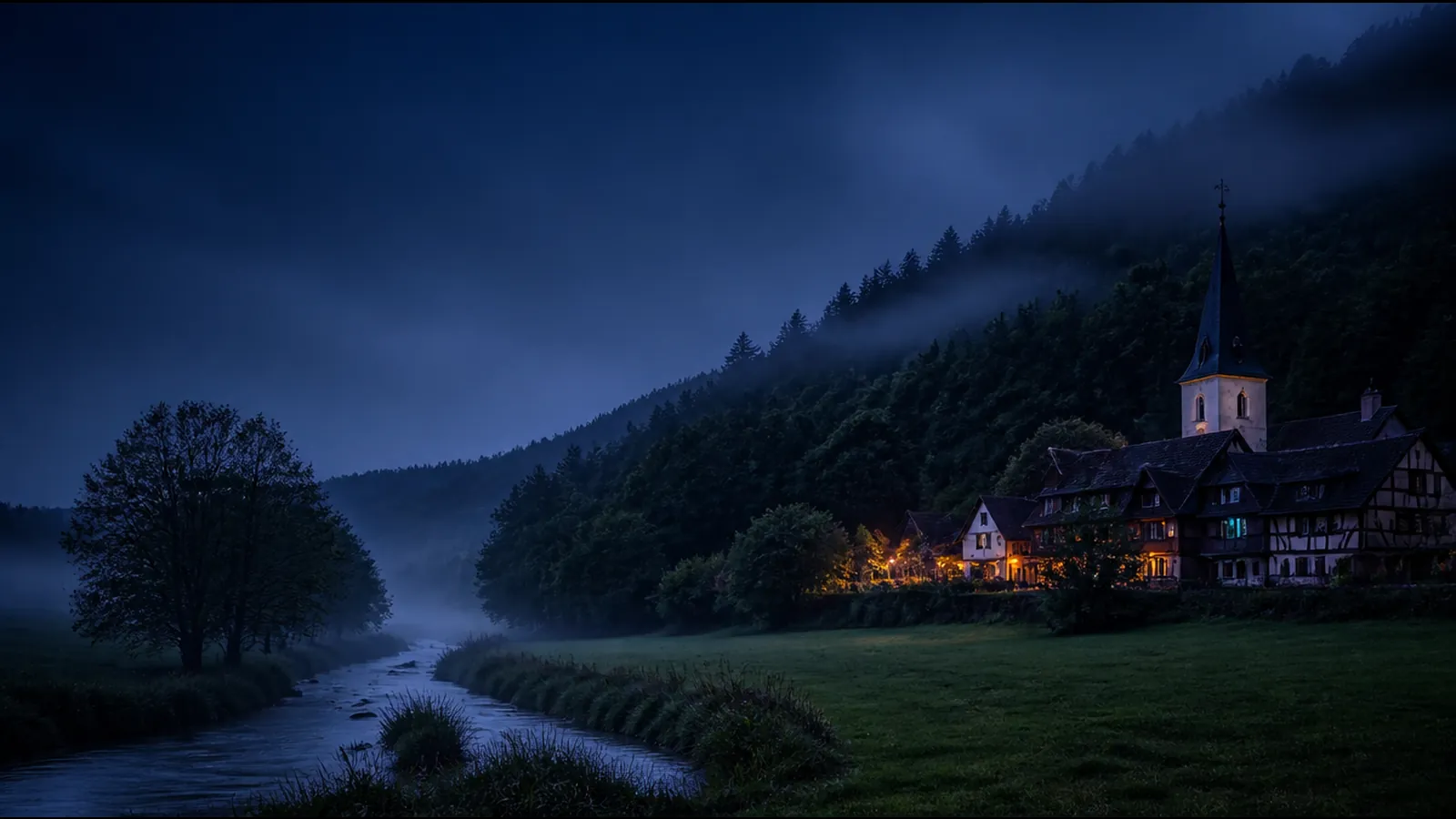 Dorf im Biebertal im Spessart zur blauen Stunde: Fachwerkhäuser und Kirche am Bachlauf, bewaldete Hügel im Nebel