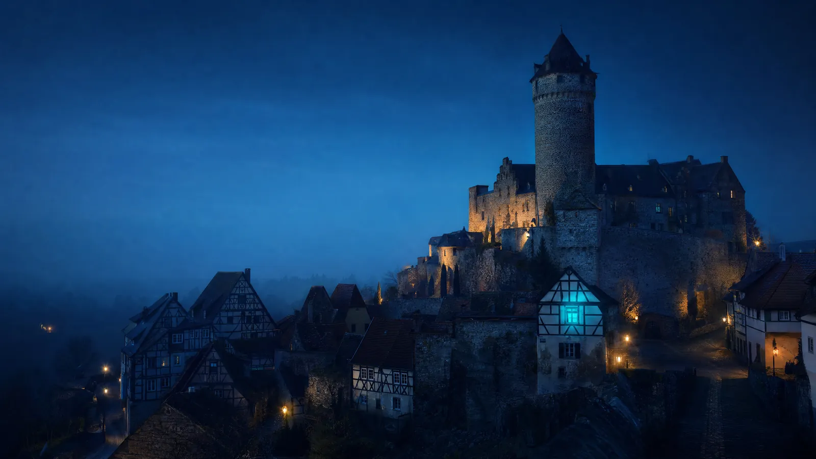 Renaissance-Schloss mit Rundturm über Fachwerkhäusern zur blauen Stunde